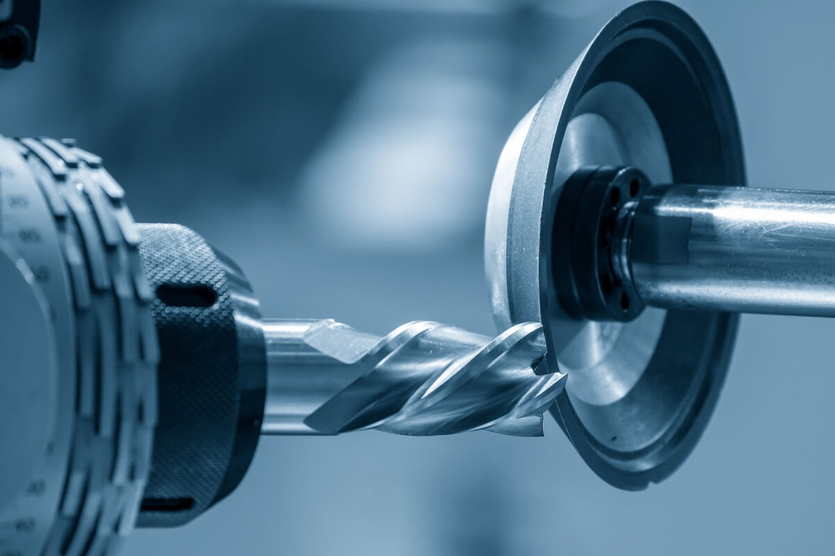 Close-up of a metal drill bit being sharpened by a grinding machine with carbide grinding blades.