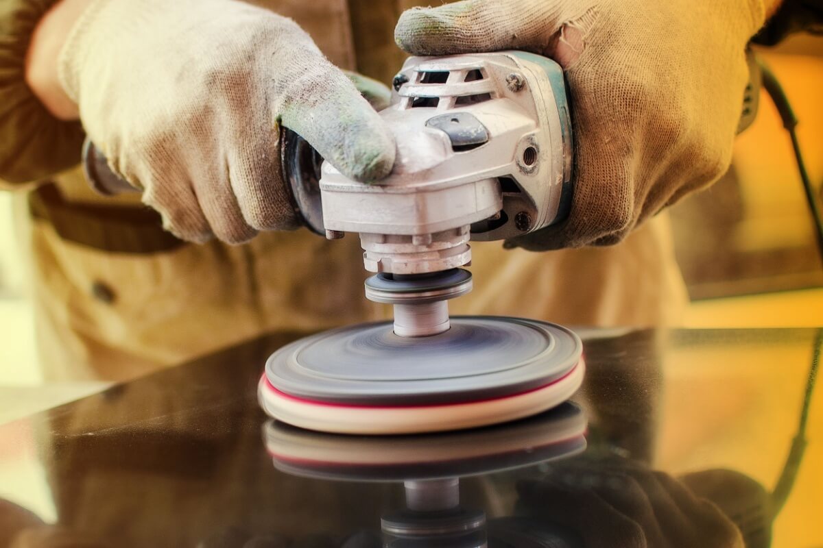 A person wearing gloves efficiently utilises an electric buffer to polish a surface, achieving a smooth finish.