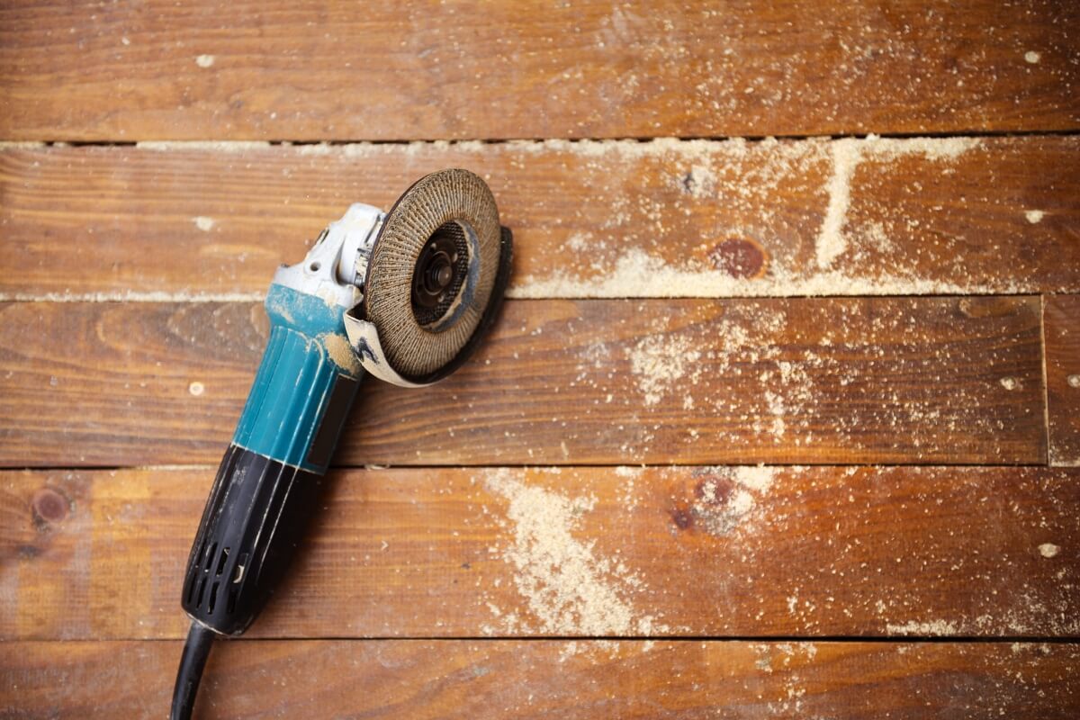An angle grinder rests on a wooden surface, surrounded by scattered sawdust.