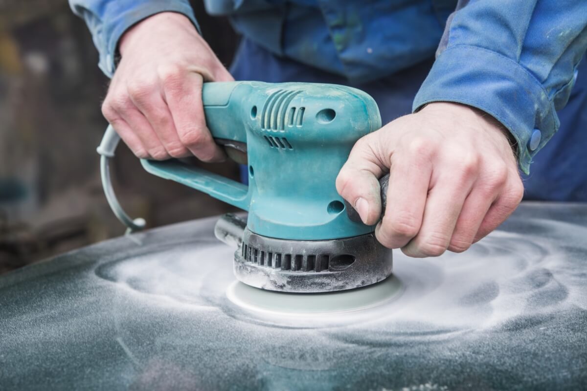 A person expertly using an electric sander, smoothing the material with circular motions, aided by high-quality abrasives.
