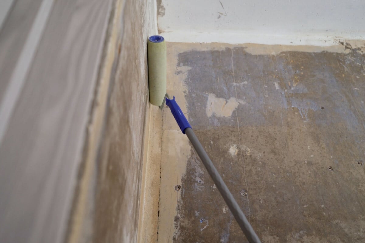 A paint roller, saturated with quality products, smoothly applies primer to a wall and the corner of a ceiling.