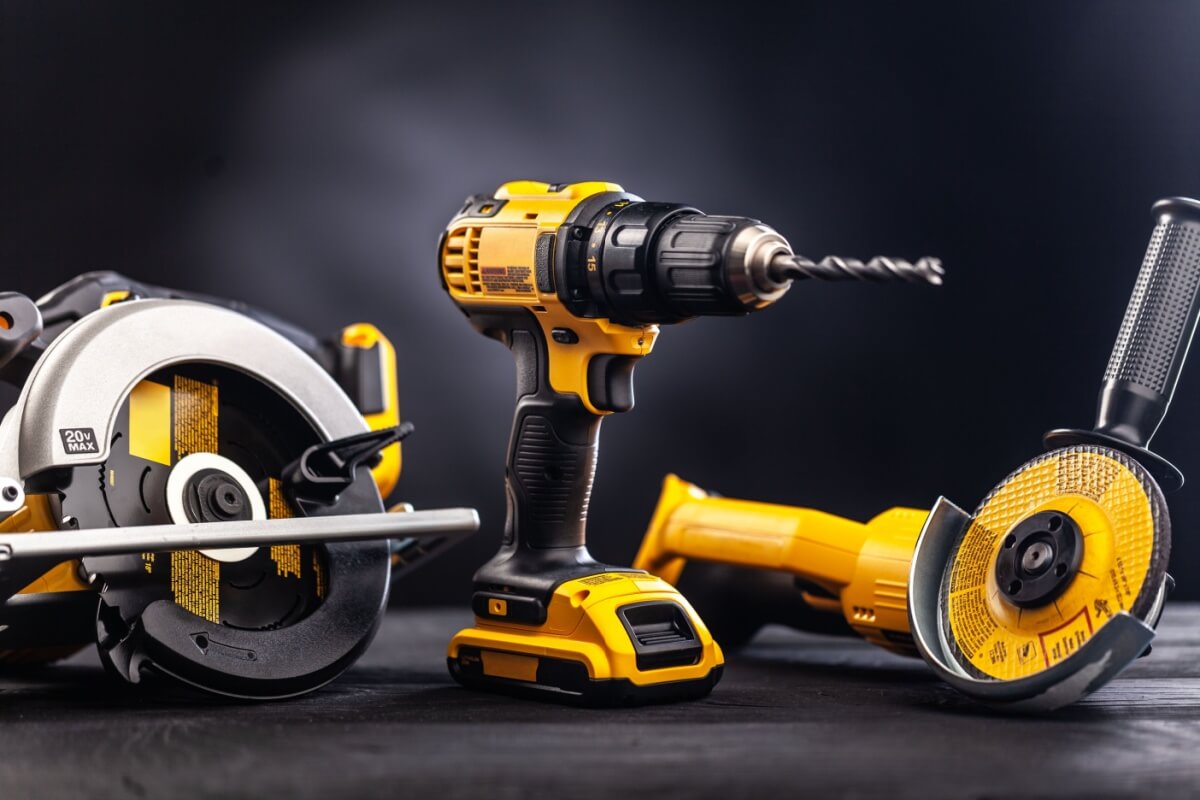 A power drill, circular saw, and angle grinder with yellow and black designs are arranged on a dark surface, complemented by various abrasives.